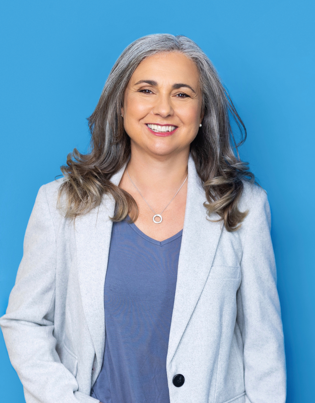 ana clements in a light grey suit with a blue v-neck top beneath. She is smiling.